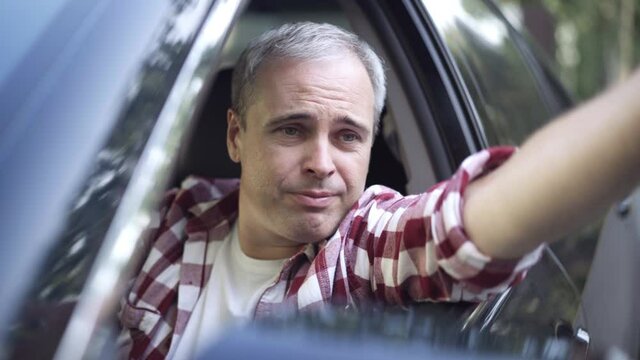 Portrait of angry man talking and gesturing out of side window sitting on driver's seat in car. Close-up of dissatisfied Caucasian driver in traffic jam. Conflict concept.