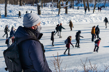 Man wearing protection mask during Covid-19 Pandemic looking at ice skaters