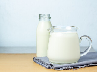Pure milk drinks in clear jars and bottles are naturally healthy foods placed on a gray cloth on a blue background.