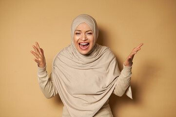 Arab muslim woman in hijab posing at camera on beige background expressing rage and irritation....