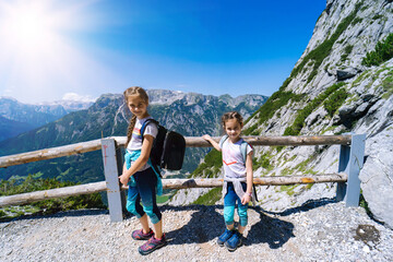 Fototapeta na wymiar Children hiking on beautiful summer day in alps mountains Austria, resting on rock and admire amazing view to mountain peaks. Active family vacation leisure with kids. Outdoor fun and healthy activity