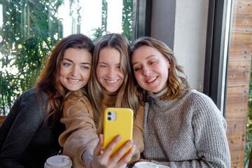 three  joyful funny girls taking a selfie while sitting together in a cafe