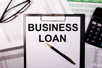 BUSINESS LOAN is written on a white sheet of paper, near the glasses and the calculator.