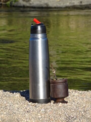 Mate argentino con termo de metal al costado del rio en playa de arena