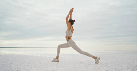 Fototapeta na wymiar Slim body yoga woman doing exercise on salt lake coast with beautiful nature view, making warrior pose. Concept wellness and harmony