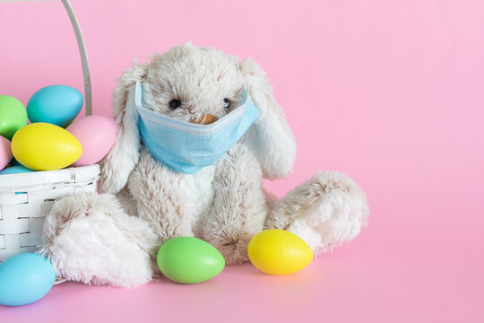 Easter bunny in mask and colored eggs in basket on pink background. Ester holiday during corona virus concept.