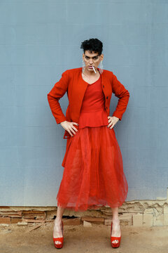 Transgender woman in red clothing, posing and smoking, with an wall of the street background. Lgtb and fashion concept.