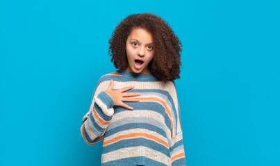  feeling shocked, astonished and surprised, with hand on chest and open mouth, saying who, me?