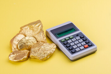 New and retro objects in business concept: A vintage calculator with digital display and a group of real raw gold pieces on Pantone 2021 yellow background. Counting value. Economy and finance