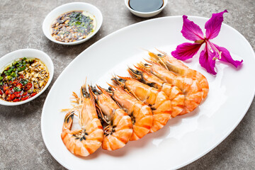 A plate of boiled black tiger prawns and seasoning sauce on cement shading
