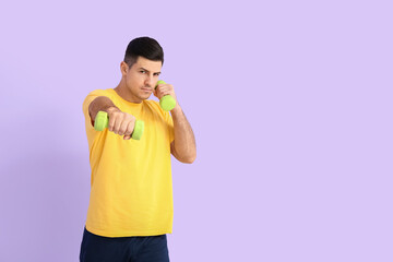 Sporty young man training with dumbbells on color background