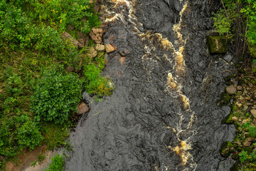 A stormy forest river, surrounded by green grass and rocks. Top view