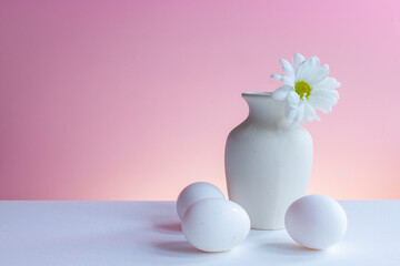 Fototapeta na wymiar White vase with white chrysanthemum and eggs on white table top on a pink background, minimalist still life. Copyspace