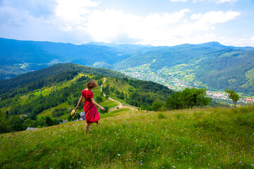 Fototapeta na wymiar Beautiful girl the mountains. Woman in linen dress and straw hat travelling. Amazing summer nature around. Harmony and wanderlust concept. Rustic natural style. Wind blowing for dynamic photo.