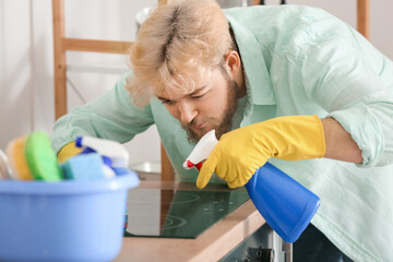 Young man cleaning infrared cooker in kitchen