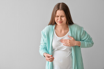 Ill pregnant young woman with pill on grey background