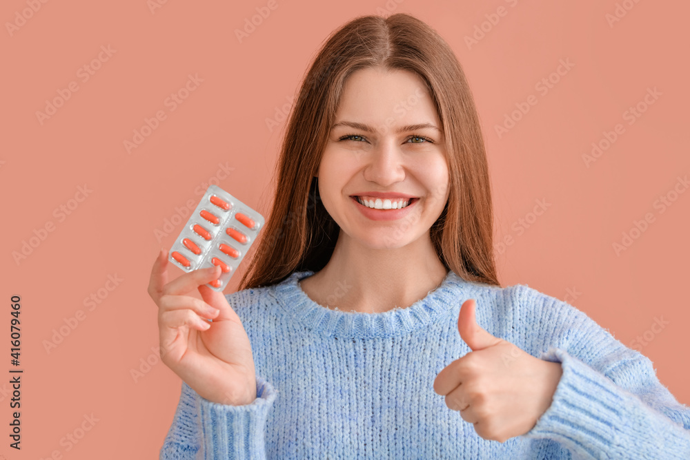 Sticker beautiful young woman with pills showing thumb-up gesture on color background