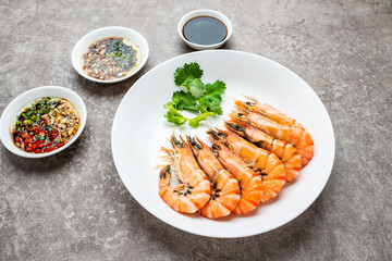 A plate of boiled black tiger prawns and seasoning sauce on cement shading