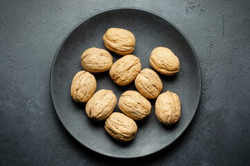 Walnuts in a plate on a dark concrete background. Nuts are a source of vegetable protein and...