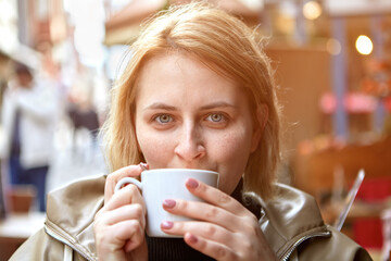 Young caucasian woman drinking tea in street cafe during cold weather.