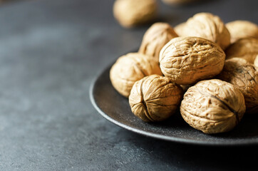 Walnuts in a plate on a dark concrete background. Nuts are a source of vegetable protein and vitamins. Copy space, selective focus