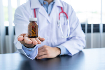 A doctor or pharmacist sits at a desk, holds or shows a bottle of medicine in his hand and writes a prescription explaining its properties. Concept of medical treatment, pharmacy or health insurance