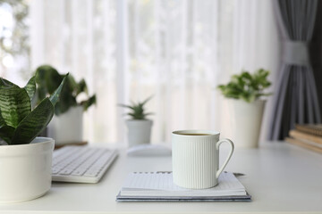 small white coffee cup with notebook and plants