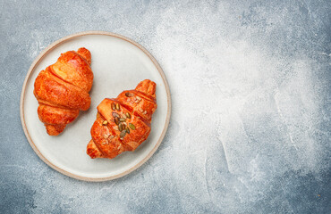 Freshly baked homemade croissants for breakfast. Traditional and whole-grain croissant with pumpkin seeds in a gray plate on a concrete or stone background. Selective focus, copy space