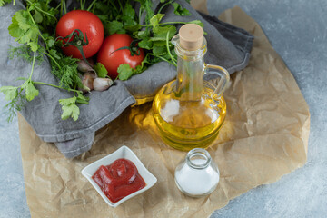 A bottle of oil with vegetables and salt on a parchment paper