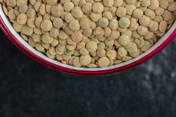 A red bowl with dried brown raw lentils on a dark background