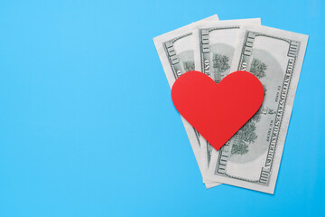 Red heart lies on American dollars on a blue background. Copy space