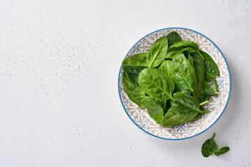 Fresh baby spinach leaves in ceramic beautiful bowl on light gray concrete background. Mock up. Top view.