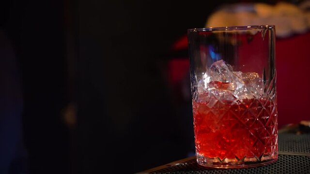 Bartender pouring cocktail Into bartending tumble with cocktail shaker on bar counter - close up