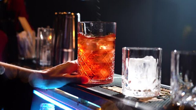 Bartender adding ice cubes and stirring in cocktail glass making cocktail in speakeasy bar