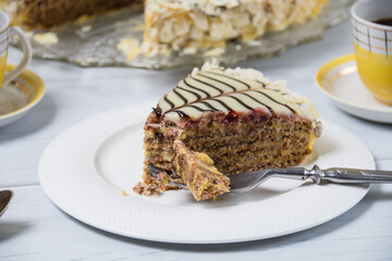 Very tasty piece of cake cut with a fork on a white plate and a cup of coffee in yellow on a light wooden table. The process of eating cake and enjoying sweet foods