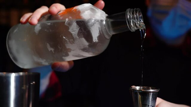 Bartender pouring cocktail Into bartending tumble with cocktail shaker on bar counter - close up