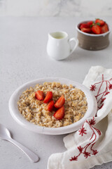 Simple oatmeal porridge with strawberries in a white plate on a linen napkin. Breakfast health food concept. Top view