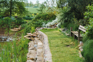 part of the garden along the edge of the pond, a wooden bench and the embankment of a pond built with stones
