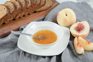 A white plate with peach jam and slices of brown bread