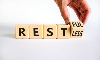 Restless or restful symbol. Businessman turns the wooden cube, changes the word 'restless' to 'restful'. Beautiful white table, white background, copy space. Business and restless or restful concept.