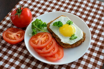 sandwich with fried egg on the white plate with tomatoes and whole grain bread on the plaid tablecloth