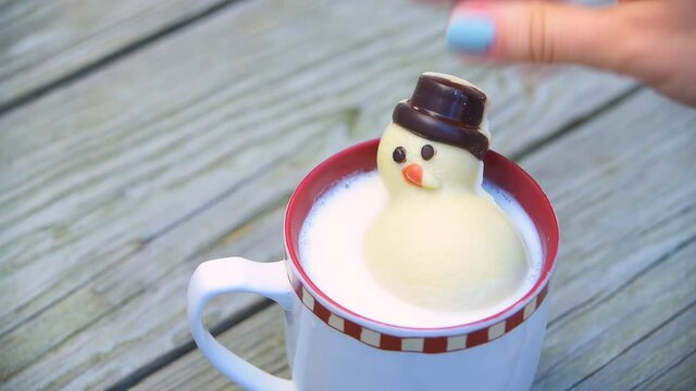 Macro closeup of one hot chocolate cup with festive marshmallow white Christmas snowman melting in milk cocoa drink on wooden table 