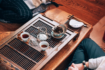 Two people are sitting on the floor next to the tea ceremony table, friends are drinking tea and talking,table with ceramic white cups and glass teapot for Chinese tea ceremony
