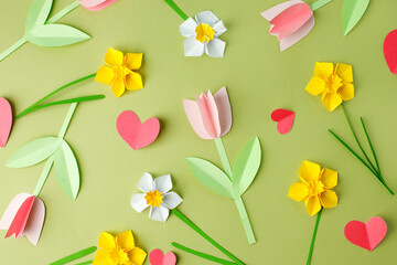 Pink origami tulips and yellow origami narcissus on green pastel background. Top view. Paper cut...