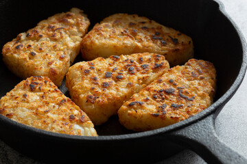 Hash browns cooked in a cast iron frying pan.  Concrete background