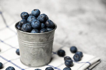 Fresh blueberries in a small metal bucket surrounded with some berries against concrete background. Top view. Rustic.