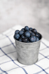 Fresh blueberries in a small metal bucket surrounded with some berries on a checked napkin. Top view. Rustic.
