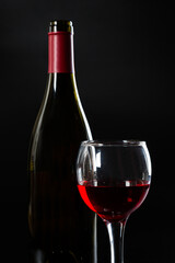 Wine bottle and glass with red wine on dark glossy background.