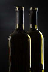 two open bottles of wine stand side by side on a dark glossy background.