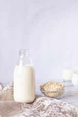 Vegetable oat milk in a glass bottle and oat flakes on a light background. Healthy drinks, vegetarianism. Side view. Vertical photo